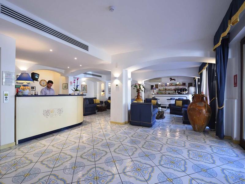 Bright hotel lobby with reception, seating areas, and large windows with curtains.