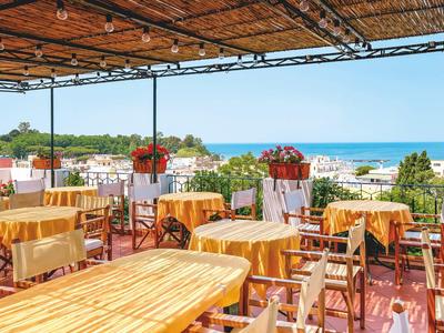 Terraza cubierta con sillas y mesas de madera con vista al mar y paisaje circundante.