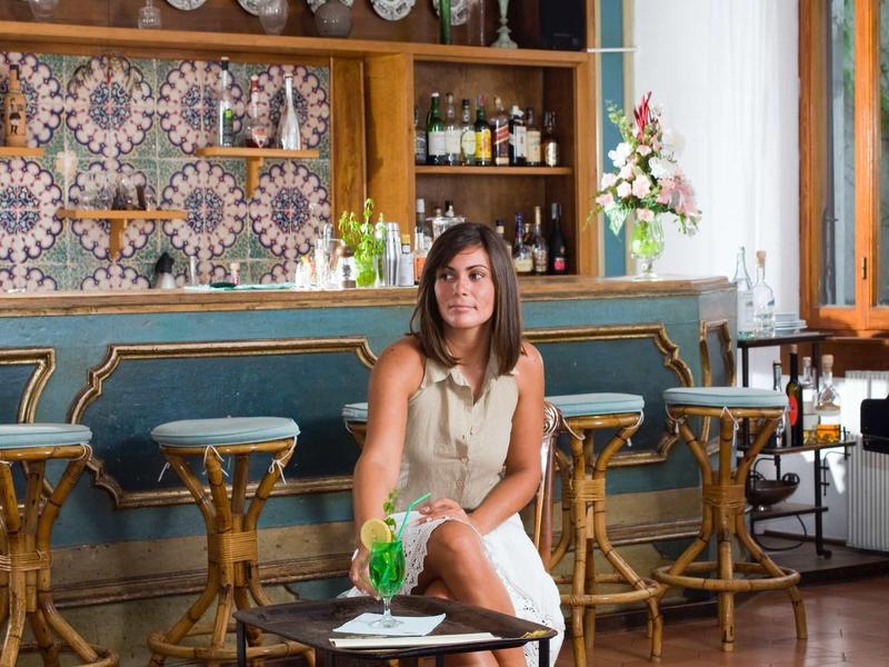 Woman sitting in stylish bar with green cocktail glass on table.