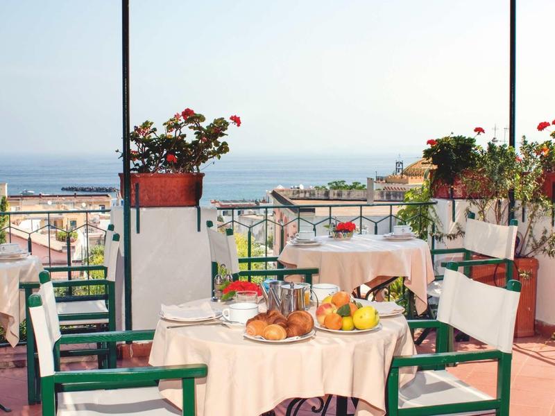 Terrace with set tables, chairs, and sea view under clear sky.