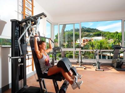 Femme s'entraîne sur un appareil de musculation dans une salle de sport avec de grandes fenêtres et vue sur les montagnes.