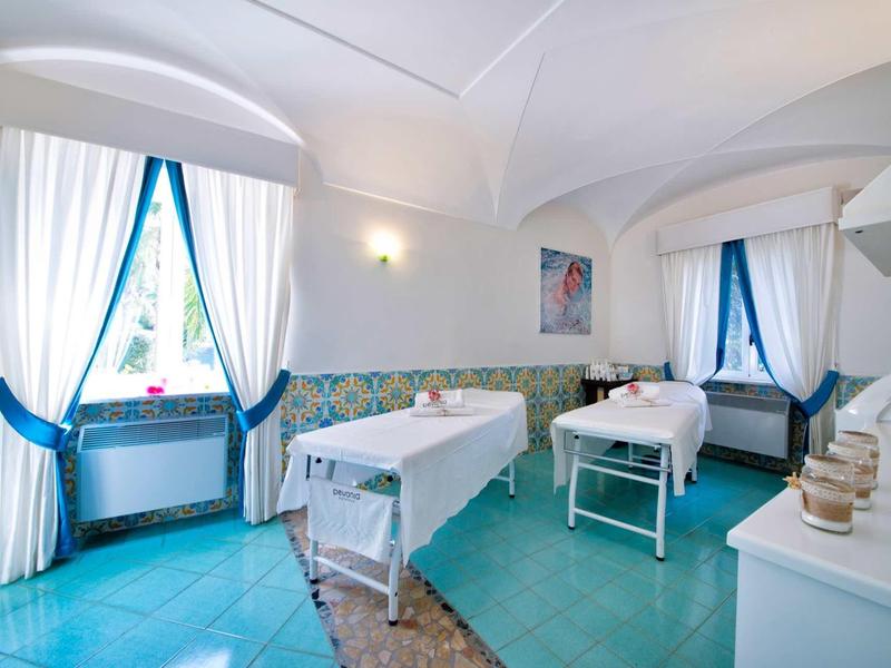 Salle de bien-être lumineuse avec deux tables de massage et des accents bleus aux fenêtres et au sol.