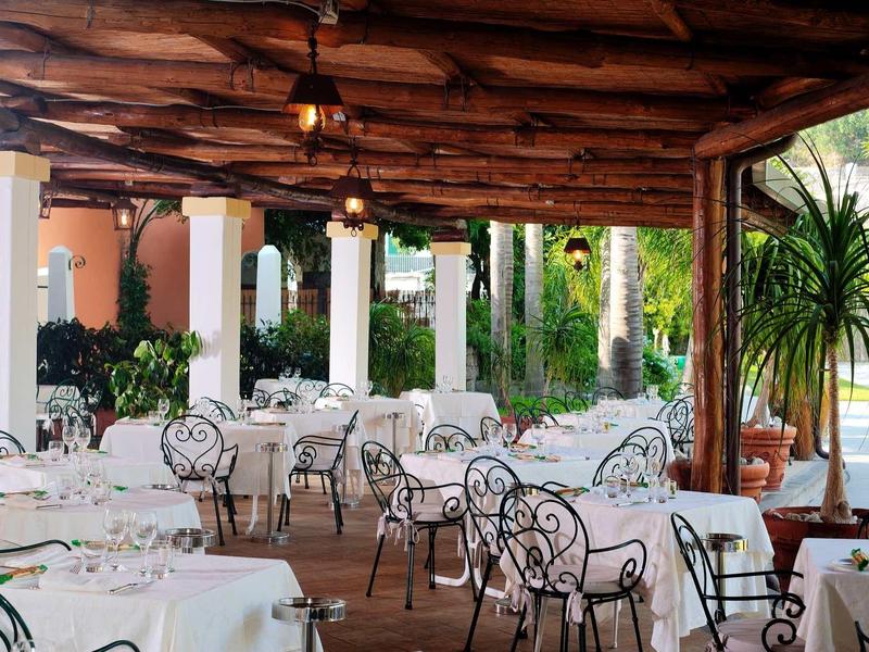 Espace extérieur couvert d'un restaurant avec des chaises en fer forgé ornées et des nappes blanches.