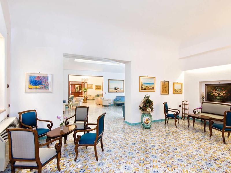 Salle commune lumineuse avec fauteuils bleus, tables et carrelage décoratif au sol.