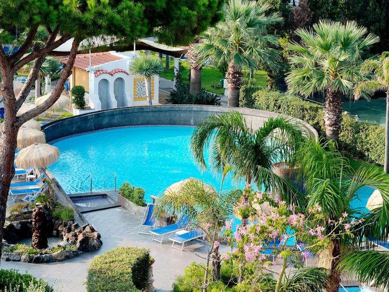 Piscine ronde entourée de jardin tropical avec des palmiers et des chaises longues.