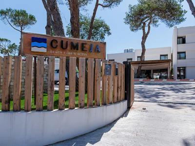 Eingang zu einem Hotel namens Cumeia mit Holzzaun und Bäumen im Hintergrund.