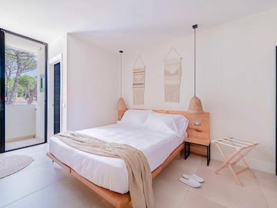 Modernes Schlafzimmer mit Doppelbett, Sandfarbenen Möbeln und Türen zu einem Balkon mit grünen Pflanzen.