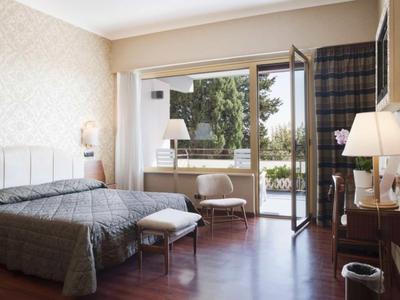 Helles Hotelzimmer mit gemütlichem Doppelbett, Sessel, Schreibtisch und Zugang zur Terrasse.