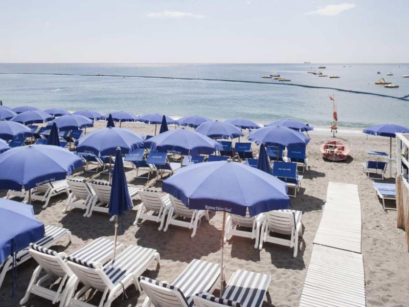 Strandgebied met veel blauwe parasols en ligstoelen aan zee.