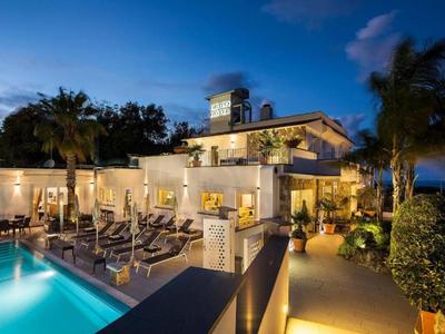 Abendansicht eines beleuchteten Hotels mit Pool und Liegestühlen im Außenbereich