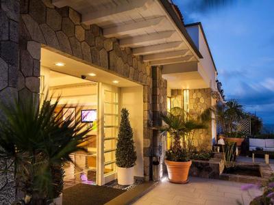 Wieczorny widok zewnętrzny nowoczesnego tarasu z roślinami i oświetlonym wejściem.