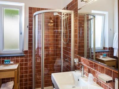 Jasna łazienka z zaokrągloną kabiną prysznicową, białą umywalką i brązowymi płytkami.