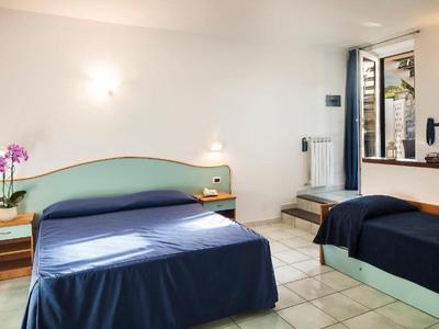 Jasny pokój hotelowy z dwoma łóżkami, kaflową podłogą i otwartym oknem z widokiem na balkon.