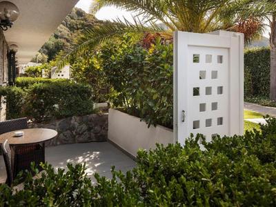 Terrasse eines Hotels mit einem kleinen Tisch, offenen weißem Tor und üppiger grüner Vegetation.