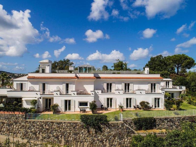 Nowoczesny budynek hotelu z balkonami i zadbanym ogrodem pod niebieskim niebem.