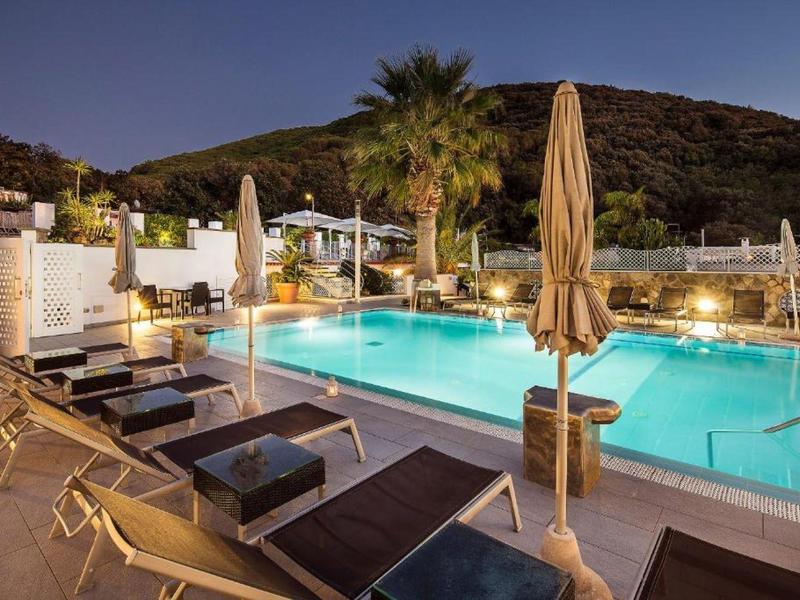 Oświetlony basen hotelowy z leżakami i parasolami wieczorem