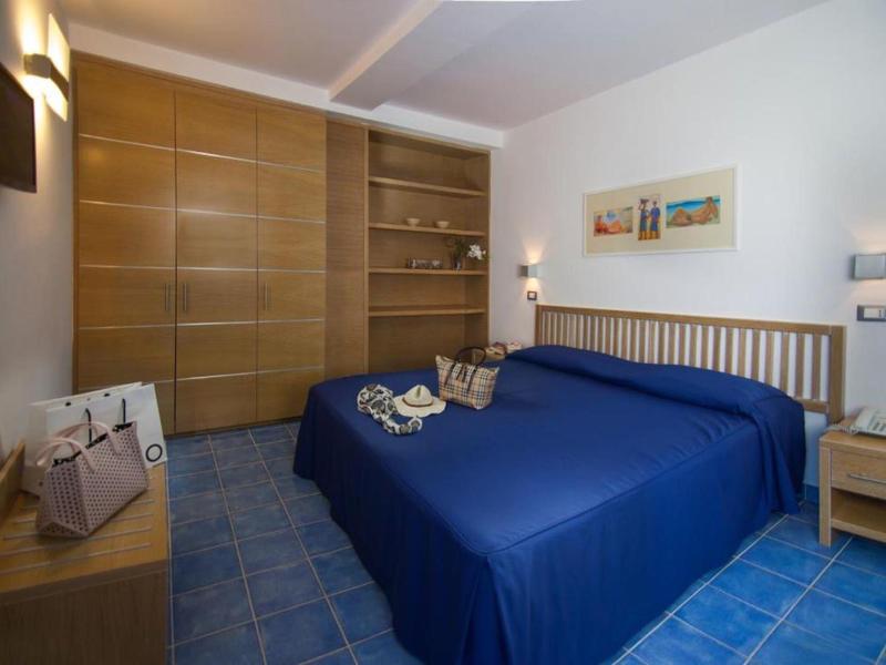 Nowoczesny pokój hotelowy z niebieskim łóżkiem, wbudowaną drewnianą szafą i niebieską podłogą z płytek.