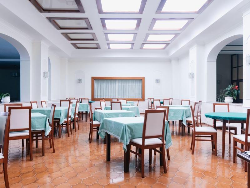 Großer heller Speisesaal mit blauen Tischdecken und Holzstühlen auf glänzendem Boden.