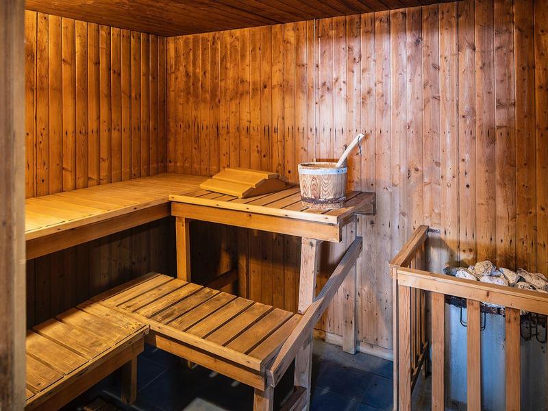Holzsauna mit mehrstufigen Sitzbänken, Saunaofen mit Steinen und Holzeimer mit Schöpfkelle.