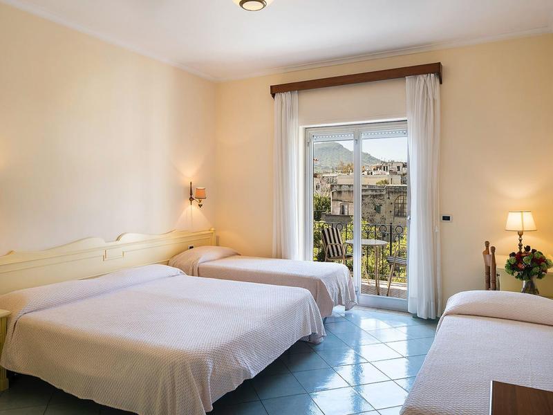 Helles Gästezimmer mit zwei Betten, Balkon, cremefarbenen Wänden und türkisfarbenem Fliesenboden.