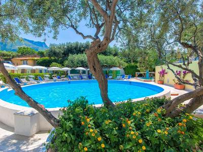 Runder Pool mit blauer Wasserfläche, umgeben von Liegestühlen und grünen Bäumen.