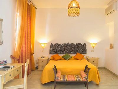 Camera luminosa con tende gialle, biancheria da letto arancione e testiera decorativa.