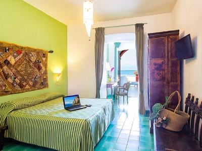 Helles Schlafzimmer mit grün gestreiftem Bett, Wandteppich, kleinem Tisch und offenem Balkon.