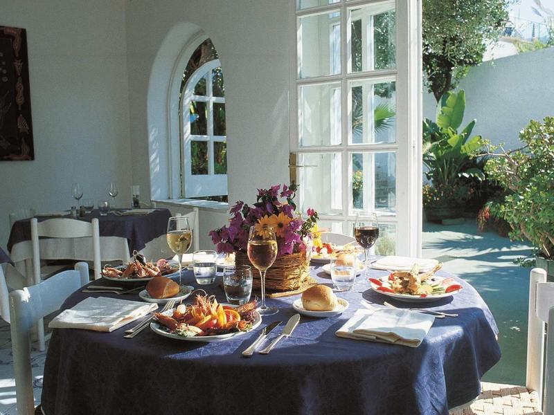 Hell erleuchteter Speiseraum mit rundem Tisch, blauem Tischtuch, gedeckt für Mahlzeit im Garten.