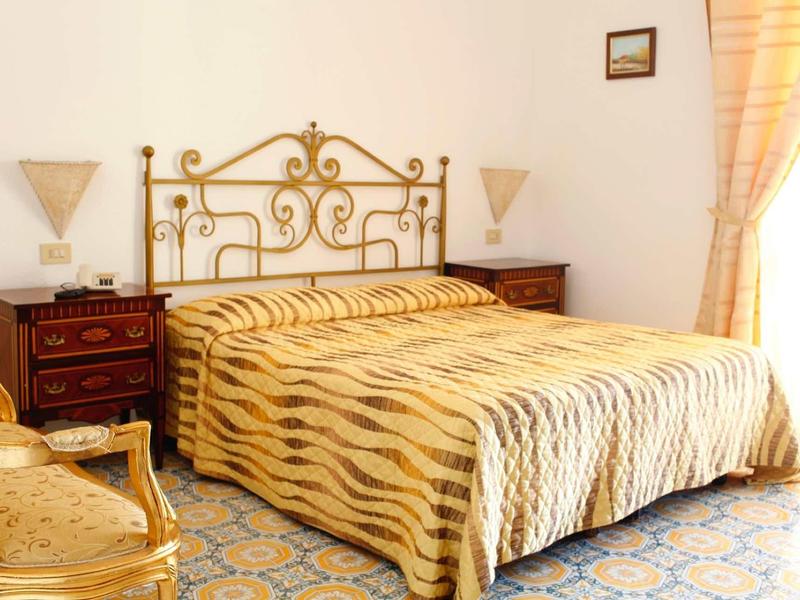 Hell eingerichtetes Schlafzimmer mit einem großen Bett, goldfarbenem Kopfteil und gemusterter Decke.