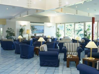 Heller Hotel-Loungebereich mit blauen Sesseln, Tischen und Lampen auf hellem Boden.