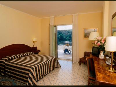 Schlafzimmer mit braun gestreiftem Bett, dunklem Holzmöbel, Lampen und offenem Balkon zur Terrasse.