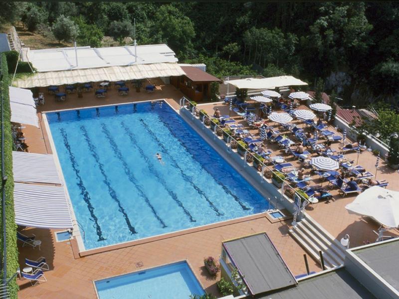 Großer blau gefliester Außenpool mit Liegestühlen und Sonnenschirmen in grüner Umgebung.