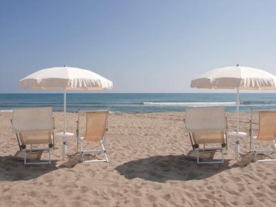 Zwei Paare von Liegestühlen mit weißen Sonnenschirmen am Sandstrand vor ruhigem Meer