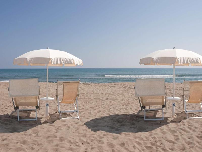 Dwa parasole plażowe z leżakami na piaszczystej plaży przy spokojnym morzu.