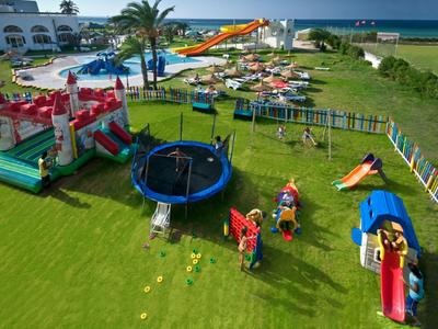 Plac zabaw dla dzieci z zjeżdżalniami, trampoliną i dmuchanym zamkiem obok hotelu i basenu przy plaży