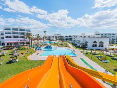 Blick von einer orangefarbenen Wasserrutsche auf einen großen Hotelpool mit Liegestühlen und Gebäuden darunter.