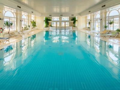 Duży jasny kryty basen z niebieskimi płytkami i roślinami na brzegach.