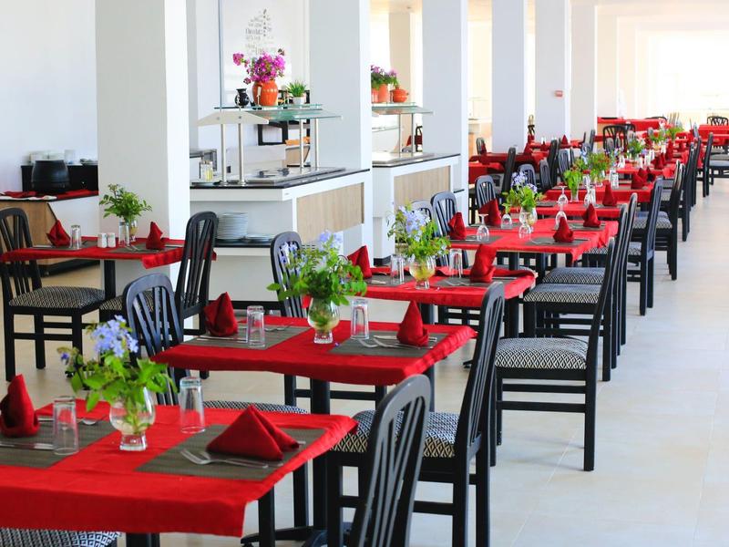 Elegant restaurant met rood gedekte tafels en zwarte stoelen in een lichte omgeving.