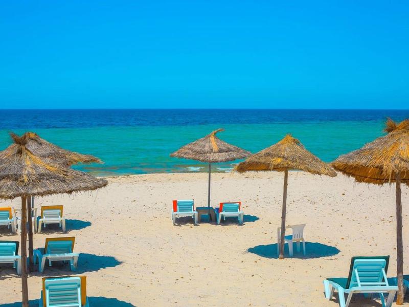 Zandstrand met ligstoelen en strooien parasols bij turquoise zee onder heldere lucht