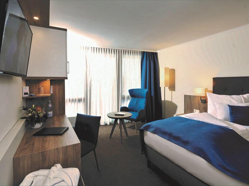 Nowoczesny pokój hotelowy z dużym łóżkiem, biurkiem i balkonem z naturalnym światłem.