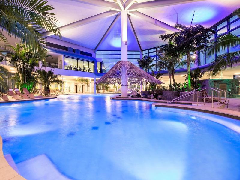 Oświetlony hotelowy basen z tropikalną atmosferą i palmami w nowoczesnym otoczeniu.