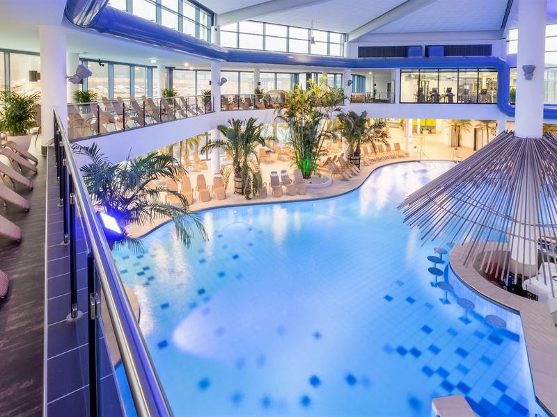 Nowoczesny basen kryty z palmami, hamakami i leżakami w jasnej części hotelu