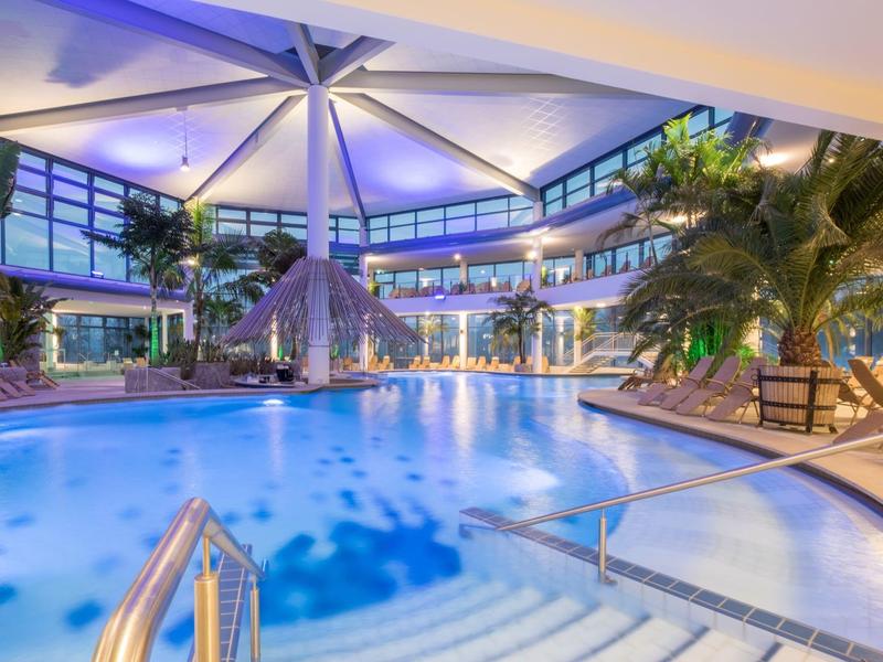 Nowoczesny kryty basen z palmami i strefami wypoczynkowymi w hotelu nocą.