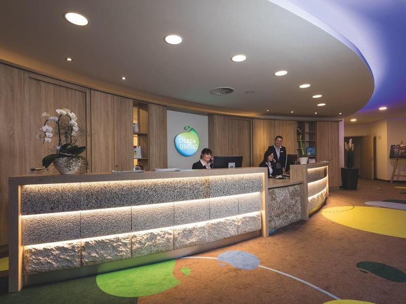 Nowoczesna lobby hotelowa z okrągłą drewniano-kamienną recepcją, oświetloną, z personelem.