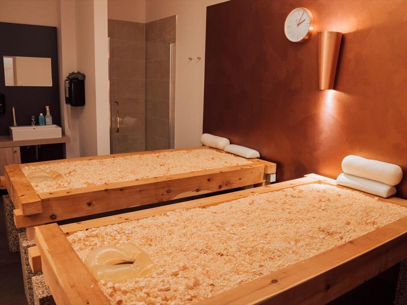 Dwa stoły do masażu z poduszkami w przytulnym, ciepło oświetlonym pokoju do zabiegów.