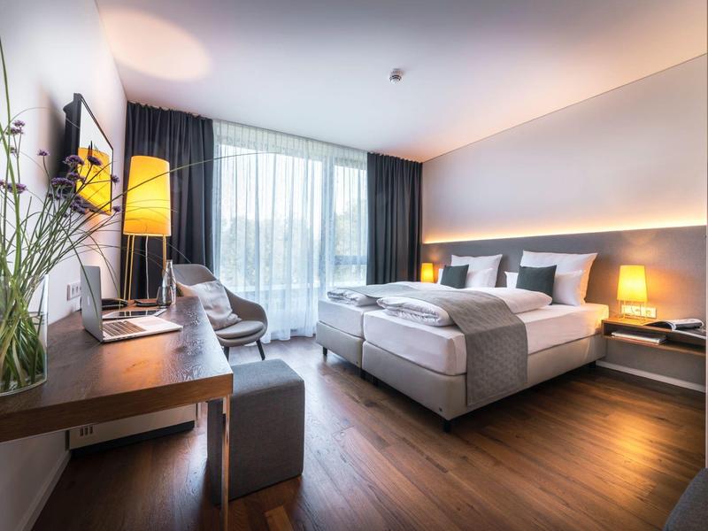 Nowoczesny pokój hotelowy z dwoma pojedynczymi łóżkami, biurkiem i przytulnym miejscem do siedzenia.