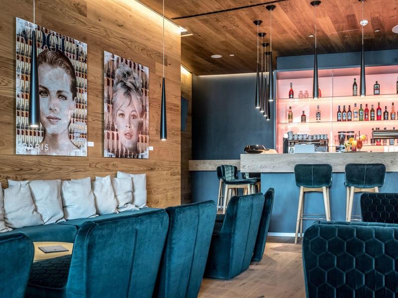 Nowoczesny bar hotelowy z niebieskimi siedzeniami, drewnianymi ścianami i dekoracyjnymi portretami.