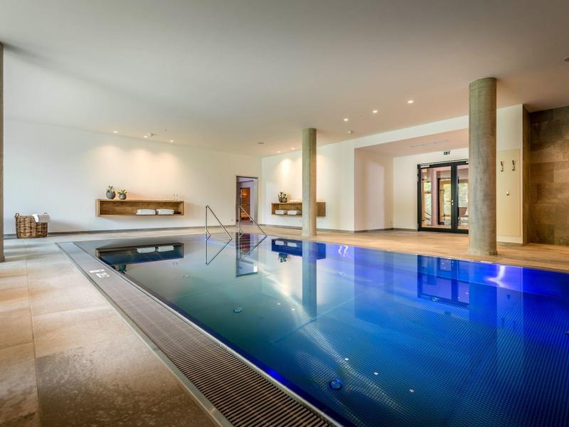 Nowoczesny kryty basen z niebieską wodą, kolumnami i ciepłym oświetleniem w hotelu.