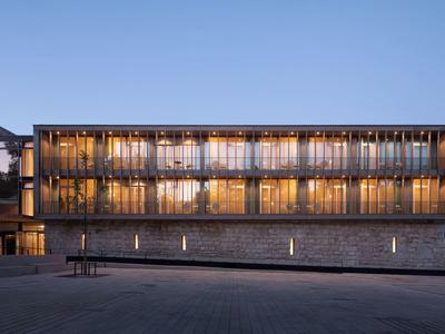 Moderní hotelová budova za soumraku s osvětlenými okny a jasnou oblohou.