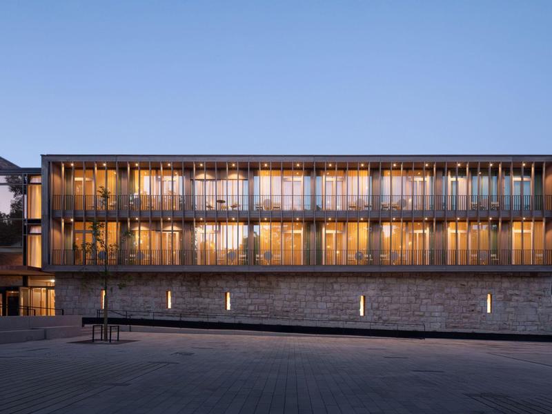 Modern hotelgebouw bij schemering met verlichte ramen en een heldere lucht.